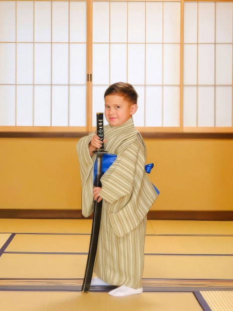 Child in kimono holding sword in traditional Japanese room.