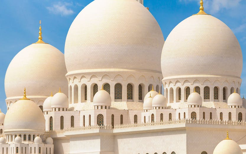 Sheikh Zayed Grand Mosque with white domes and minarets under a blue sky in Abu Dhabi.