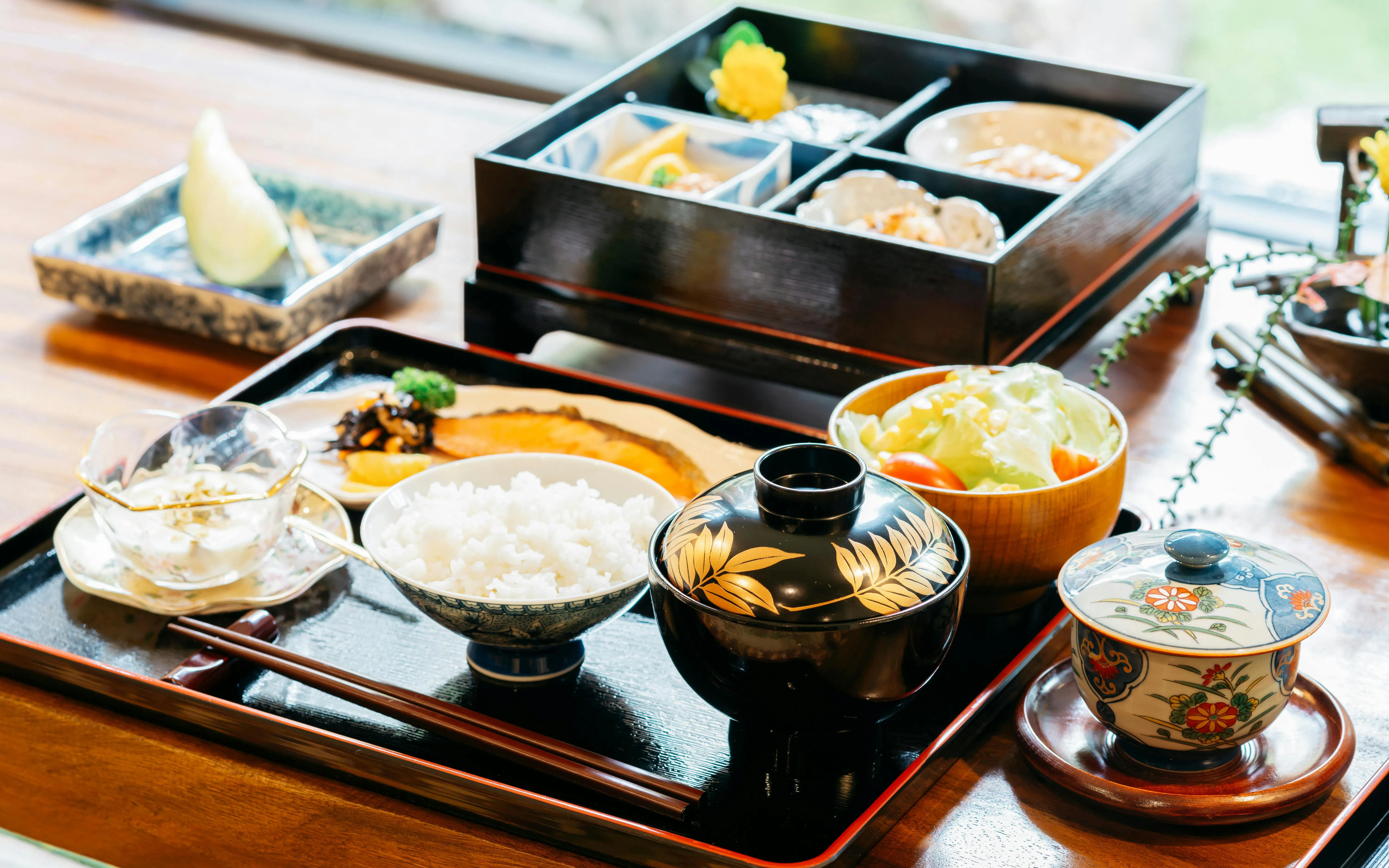 Traditional Japanese meal with rice, miso soup, and assorted dishes in a bento box.