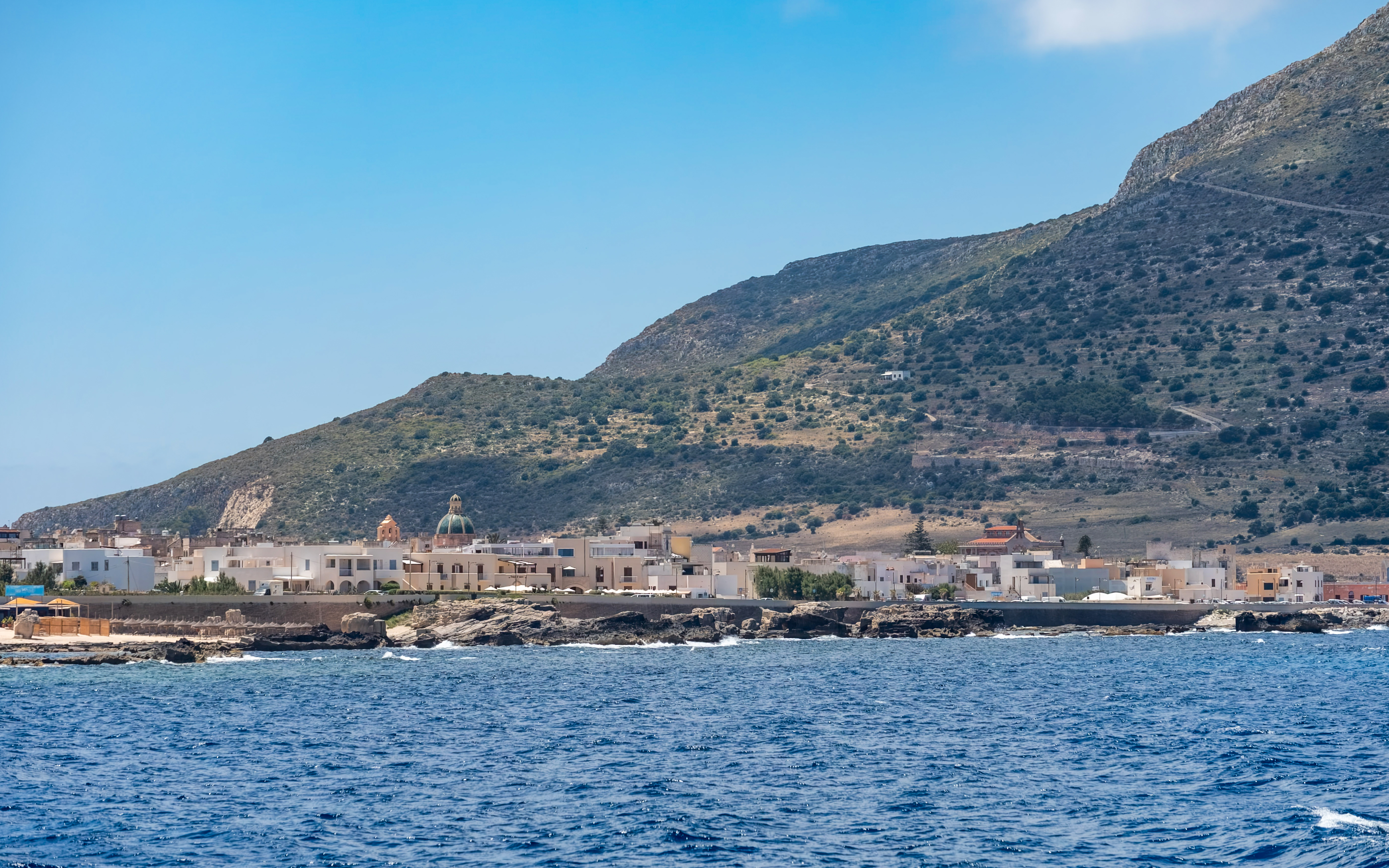 Boat trip view of Favignana island coastline with small village and hills.