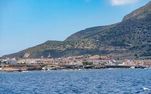 Boat trip view of Favignana island coastline with small village and hills.