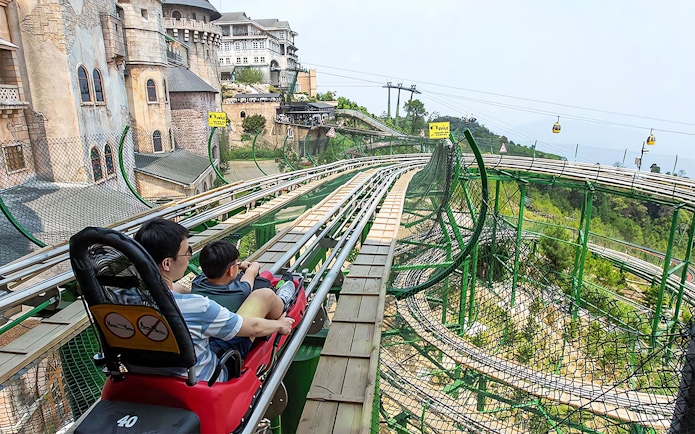 Father and child on Alpine Coaster at Ba Na Hills, Vietnam, with scenic view.