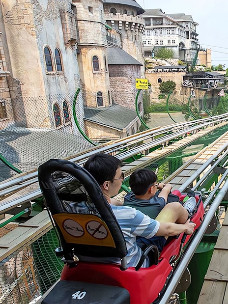 Father and child on Alpine Coaster at Ba Na Hills, Vietnam, with scenic view.