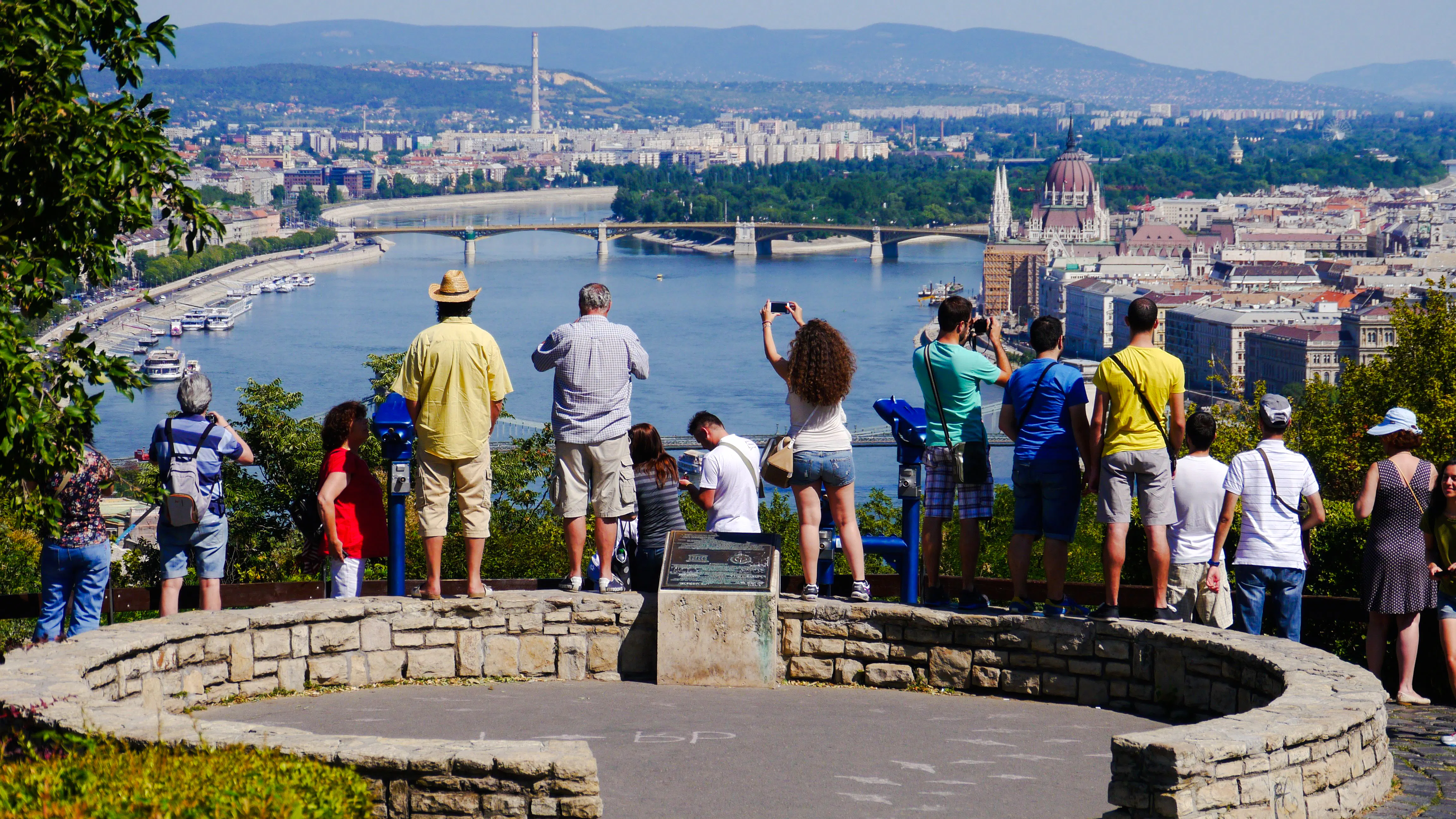 Tourists viewing Budapest skyline from Citadella with Danube River and Parliament building.