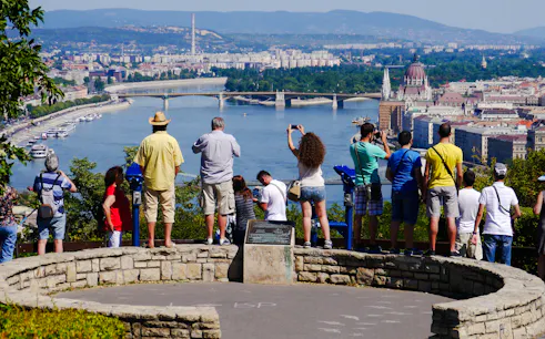 Tourists viewing Budapest skyline from Citadella with Danube River and Parliament building.