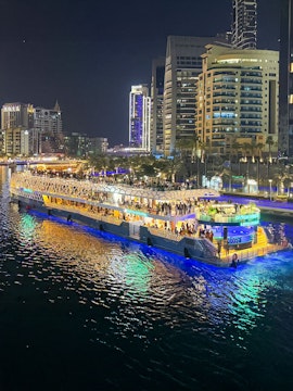 Nighttime cityscape with a lit-up cruise ship on the water, surrounded by illuminated skyscrapers.
