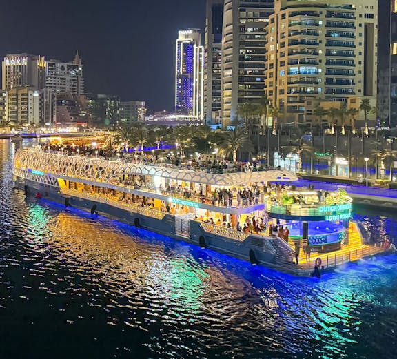 Nighttime cityscape with a lit-up cruise ship on the water, surrounded by illuminated skyscrapers.