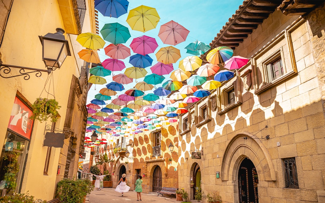 Tourists walking under colorful umbrellas in Poble Espanyol, Barcelona.