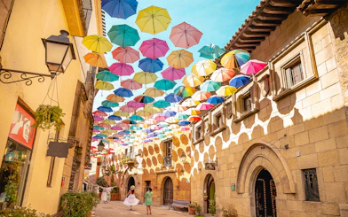 Tourists walking under colorful umbrellas in Poble Espanyol, Barcelona.