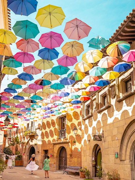Tourists walking under colorful umbrellas in Poble Espanyol, Barcelona.