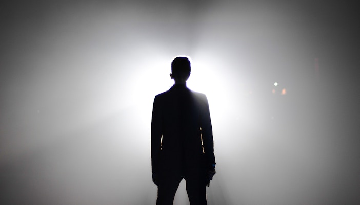 Performer on stage under spotlight during a live show in a theater.