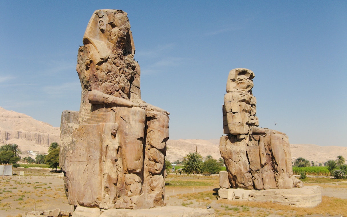 Colossi of Memnon statues on Luxor's West Bank, Egypt, with desert landscape.