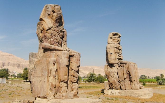 Colossi of Memnon statues on Luxor's West Bank, Egypt, with desert landscape.