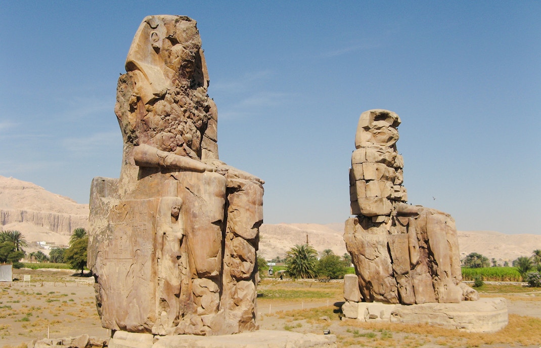 Colossi of Memnon statues on Luxor's West Bank, Egypt, with desert landscape.