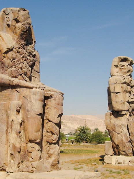 Colossi of Memnon statues on Luxor's West Bank, Egypt, with desert landscape.