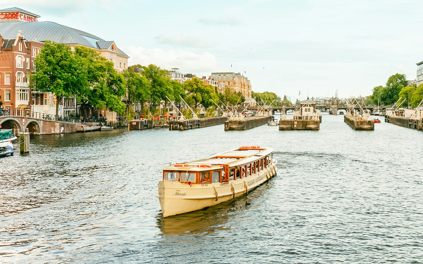 Amsterdam canal cruise boat with passengers enjoying drinks.