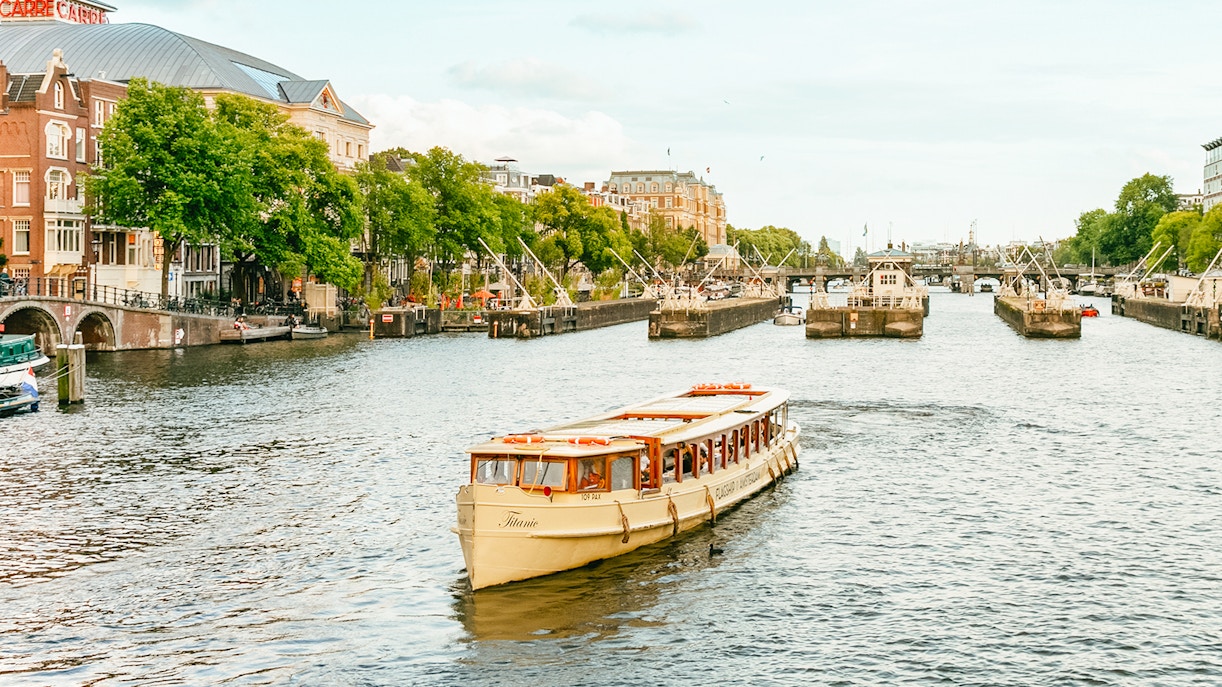 Amsterdam canal cruise boat with passengers enjoying drinks.