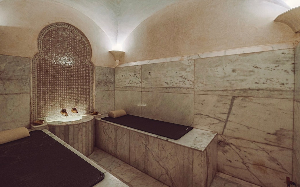 Luxury steam hammam with marble benches and ornate wall fountain.