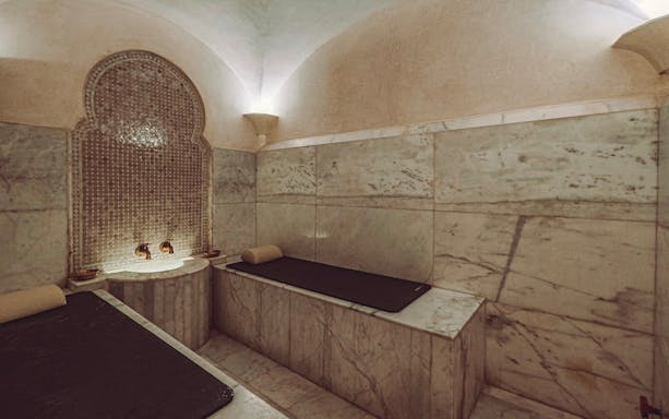 Luxury steam hammam with marble benches and ornate wall fountain.