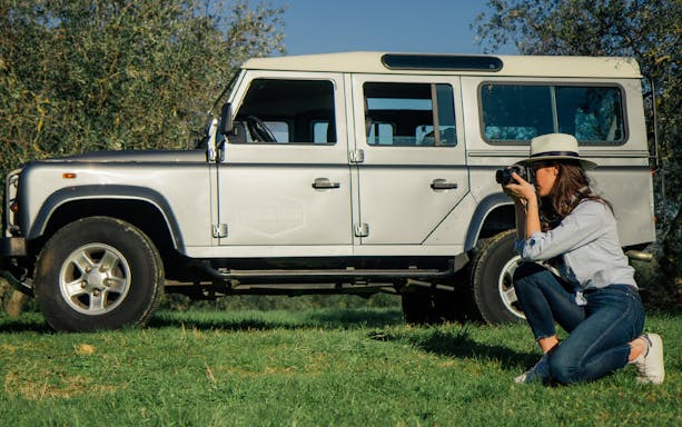 Woman photographing near safari vehicle in Tuscany vineyard.