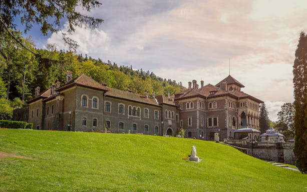 Cantacuzino Castle in Bușteni, Romania, surrounded by lush greenery.