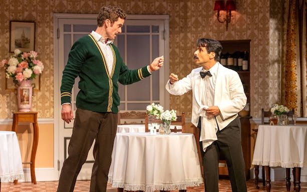 Two actors in a comedic scene from Fawlty Towers, set in a vintage dining room.