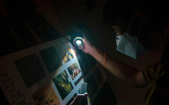 Person examining puzzle clues with flashlight in Breakout Avenue K, Chamber of Hocus, Dubai.