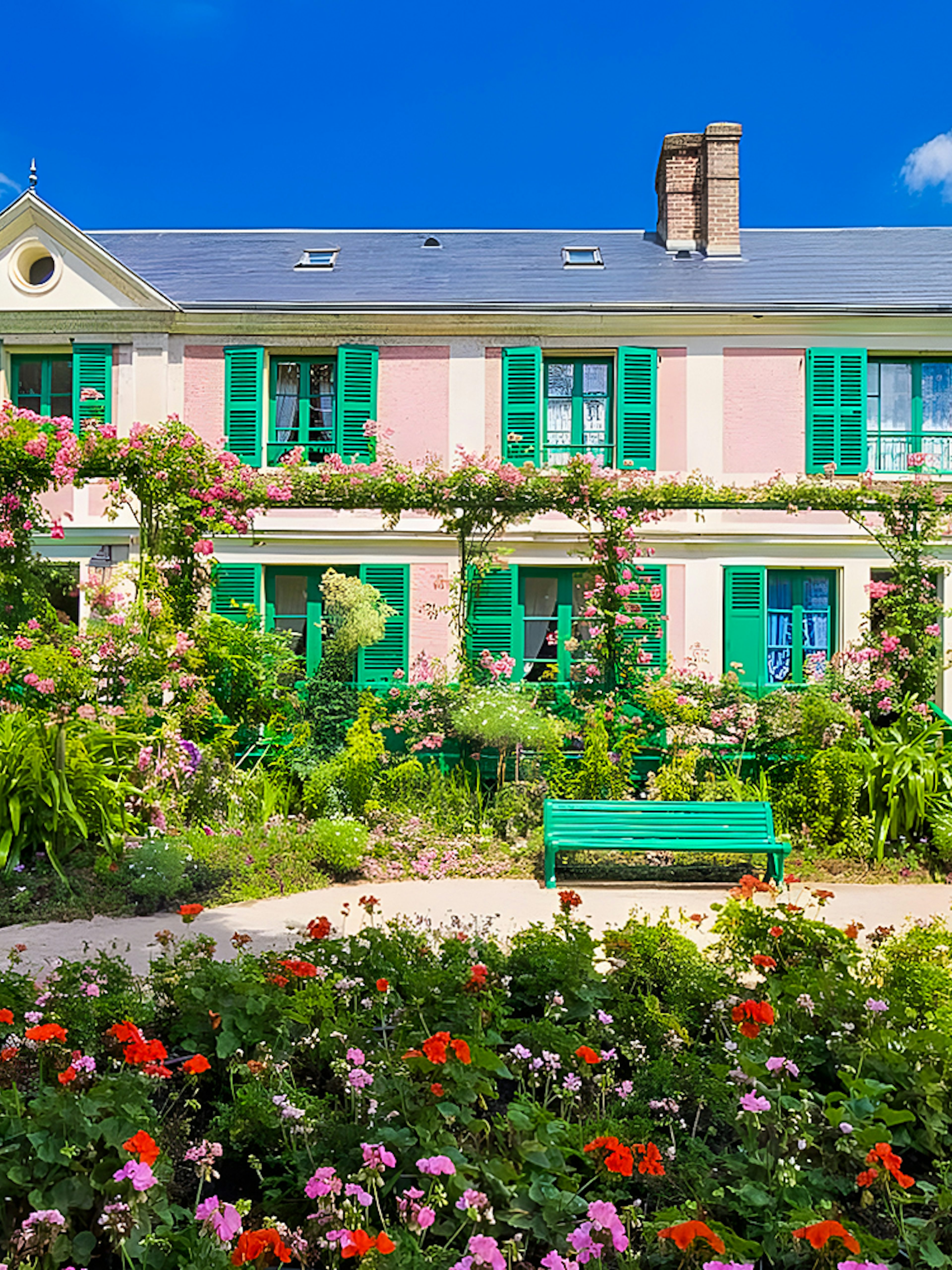 Monet's House with vibrant gardens in Giverny, France, featuring colorful flowers and green shutters.