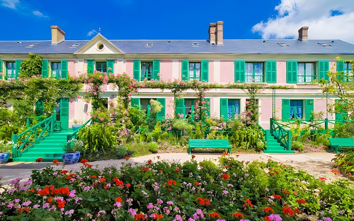 Monet's House with vibrant gardens in Giverny, France, featuring colorful flowers and green shutters.