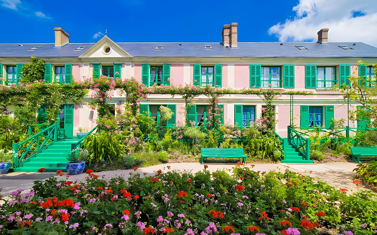 Monet's House with vibrant gardens in Giverny, France, featuring colorful flowers and green shutters.