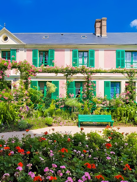 Monet's House with vibrant gardens in Giverny, France, featuring colorful flowers and green shutters.