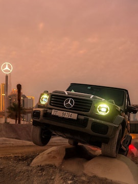 Mercedes-Benz SUV navigating terrain at sunset, Dubai skyline in background.