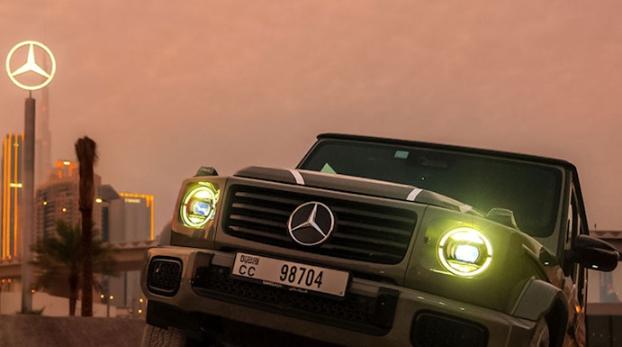 Mercedes-Benz SUV navigating terrain at sunset, Dubai skyline in background.