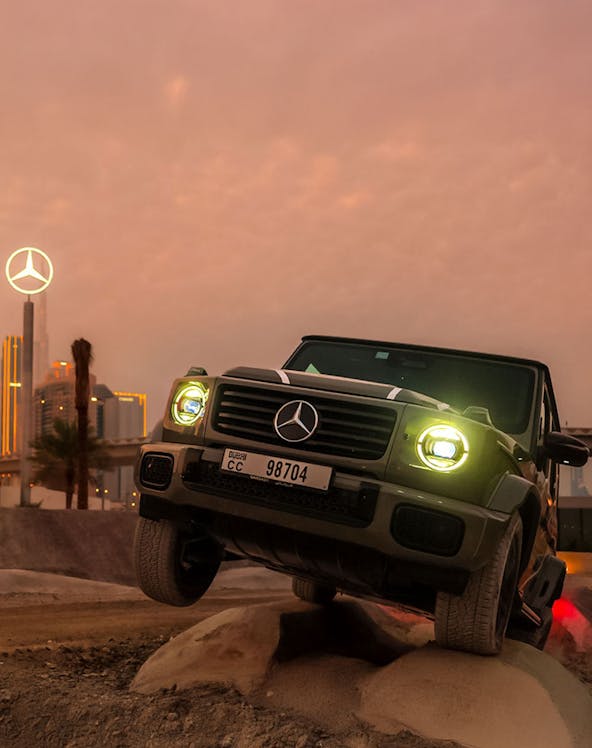 Mercedes-Benz SUV navigating terrain at sunset, Dubai skyline in background.