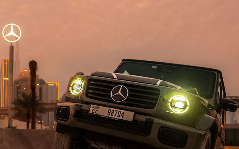 Mercedes-Benz SUV navigating terrain at sunset, Dubai skyline in background.