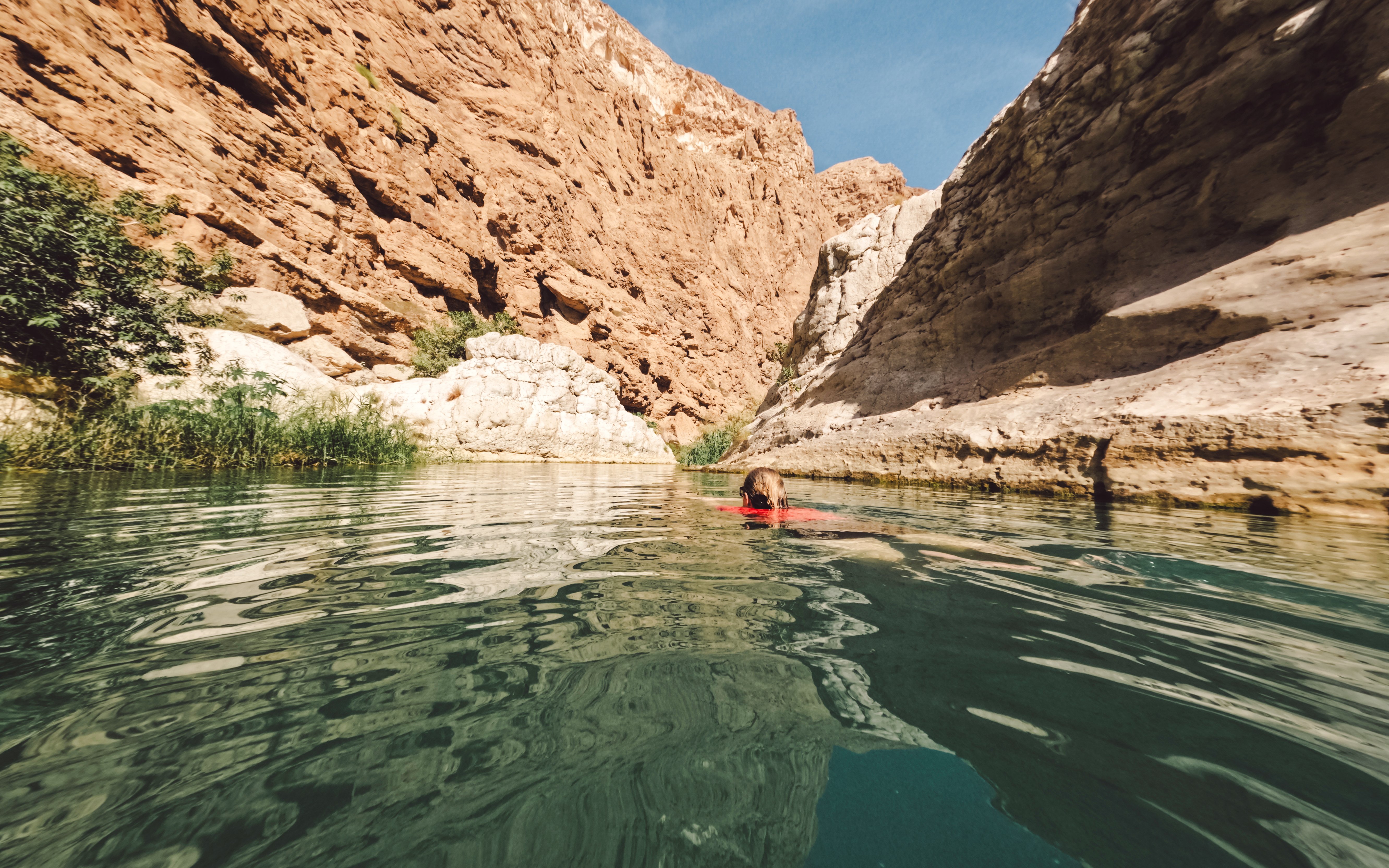 Woman swimming in clear waters of Wadi Shab, Oman, surrounded by rocky cliffs.