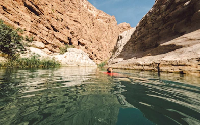 Woman swimming in clear waters of Wadi Shab, Oman, surrounded by rocky cliffs.