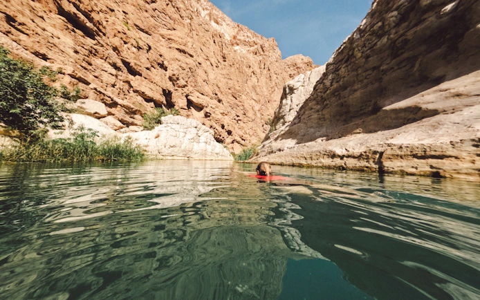 Woman swimming in clear waters of Wadi Shab, Oman, surrounded by rocky cliffs.