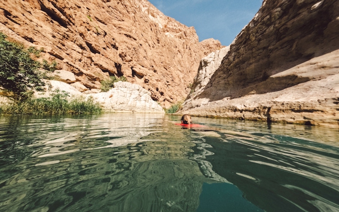 Woman swimming in clear waters of Wadi Shab, Oman, surrounded by rocky cliffs.