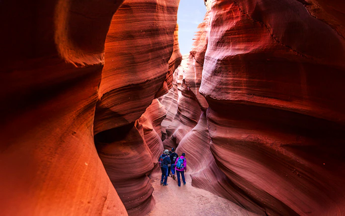 Visitors exploring narrow sandstone passage in Waterhole Canyon.