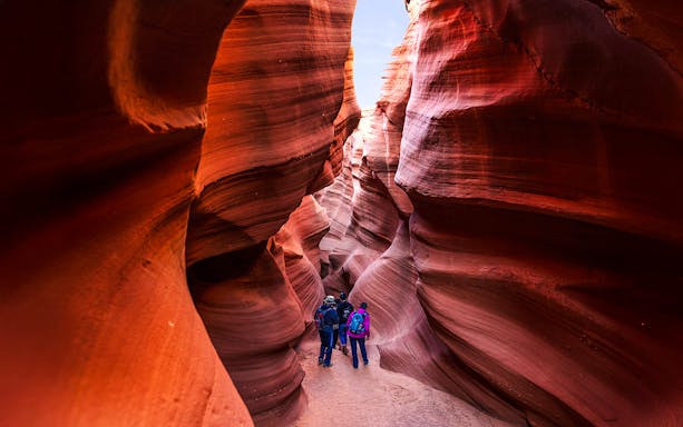 Visitors exploring narrow sandstone passage in Waterhole Canyon.