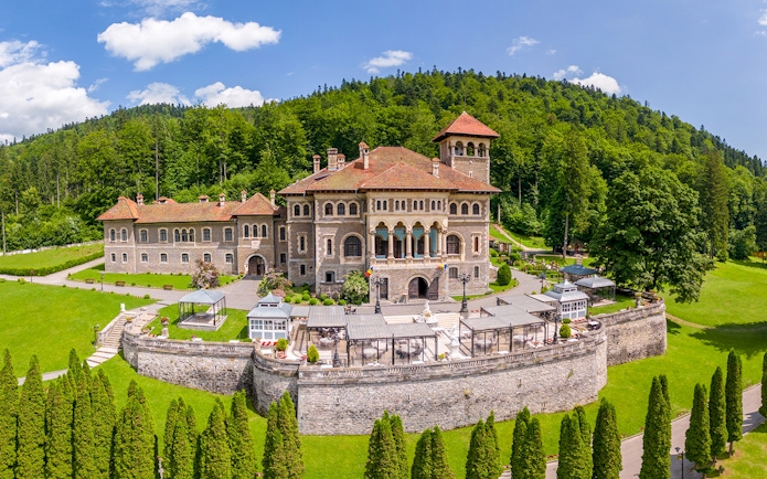 Cantacuzino Castle exterior with lush gardens and forest backdrop in Romania.