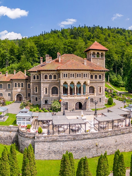 Cantacuzino Castle exterior with lush gardens and forest backdrop in Romania.