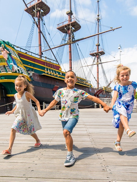 Children playing outside the National Maritime Museum with a historic ship in the background.
