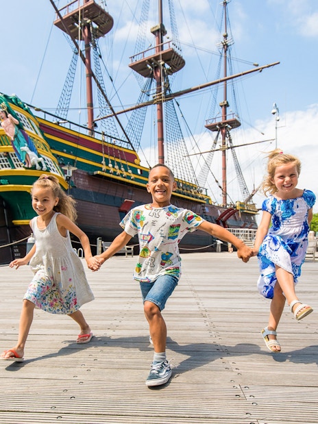 Children playing outside the National Maritime Museum with a historic ship in the background.