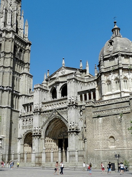 Toledo Cathedral facade with bell tower and tourists, Spain.