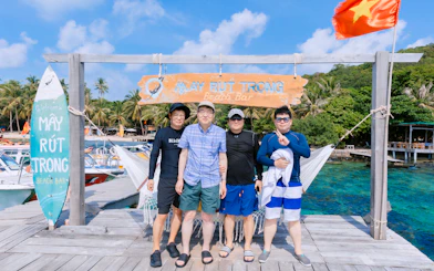 Group of tourists at May Rut Trong Beach Bar, Phu Quoc Island, with palm trees and boats in the background.