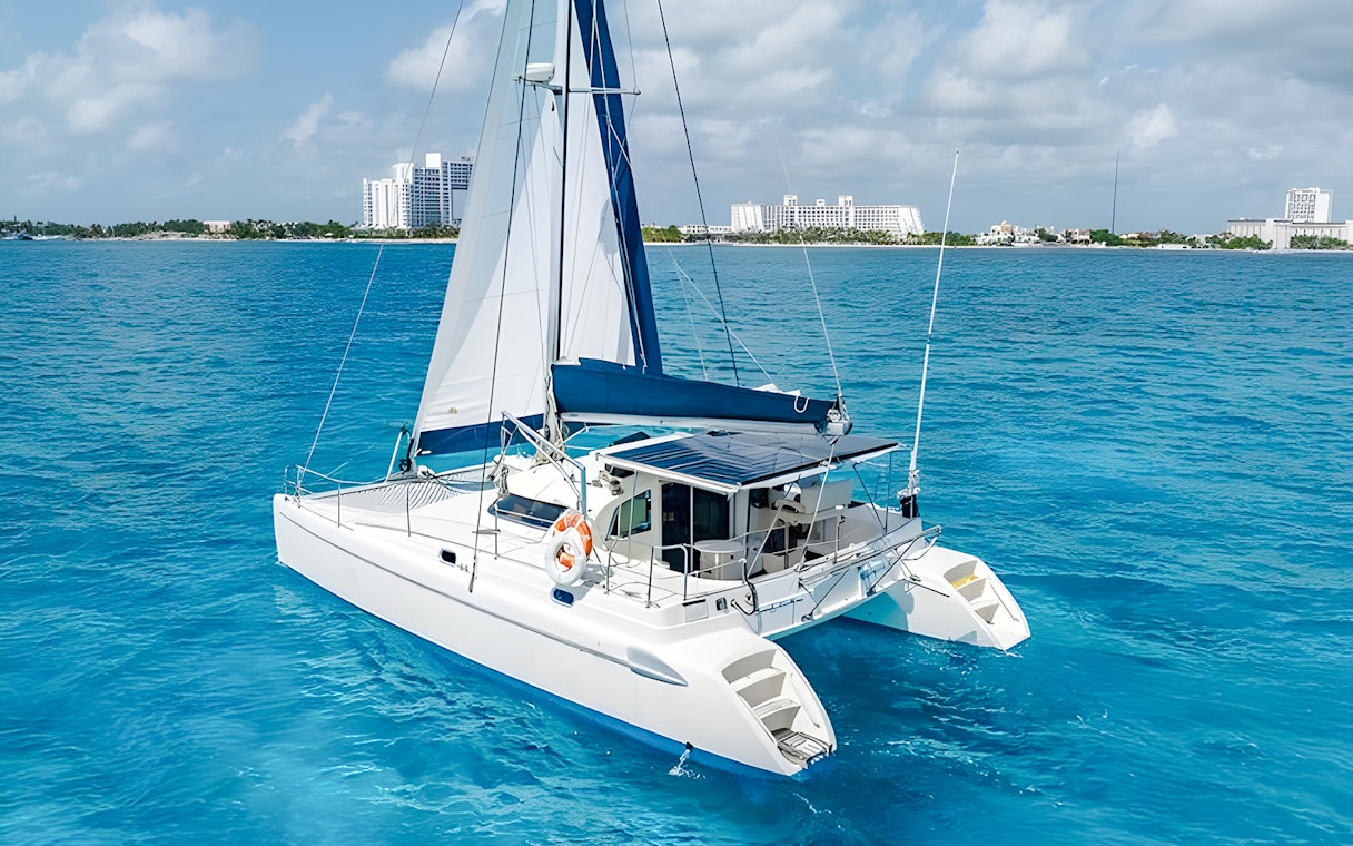 Catamaran sailing near Isla Mujeres with city skyline in the background.