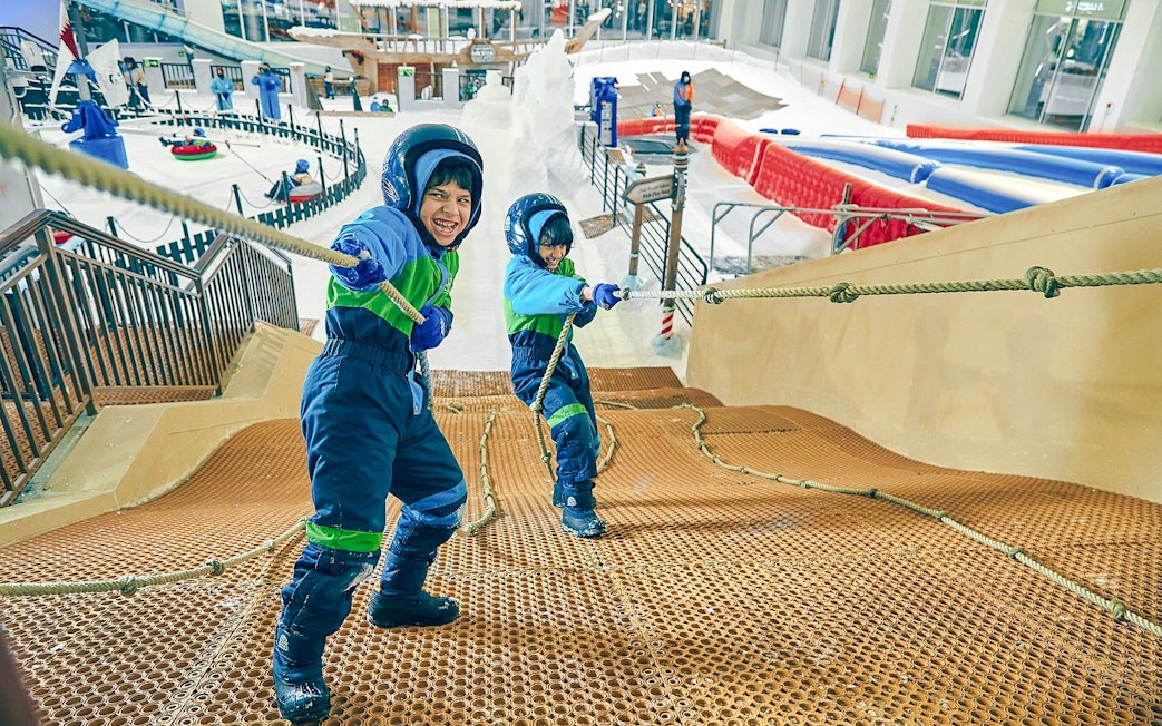 Children climbing rope hill at Snow Dunes Theme Park indoor snow area.