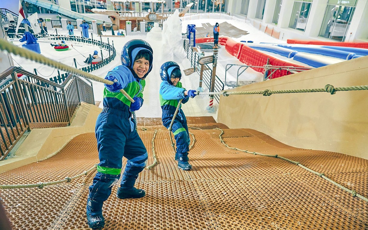 Children climbing rope hill at Snow Dunes Theme Park indoor snow area.